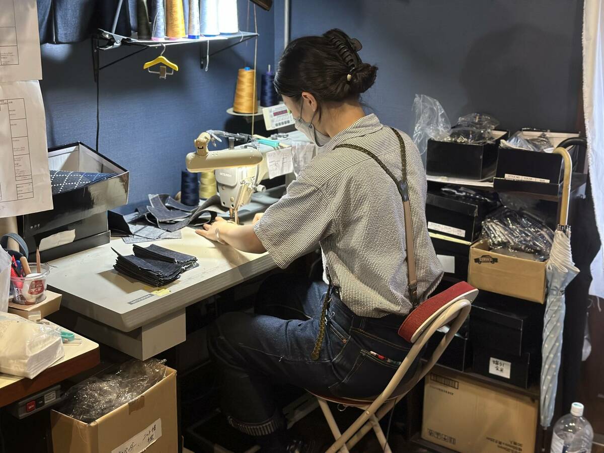 ショップ内のミシンでデニム小物を縫製する作業